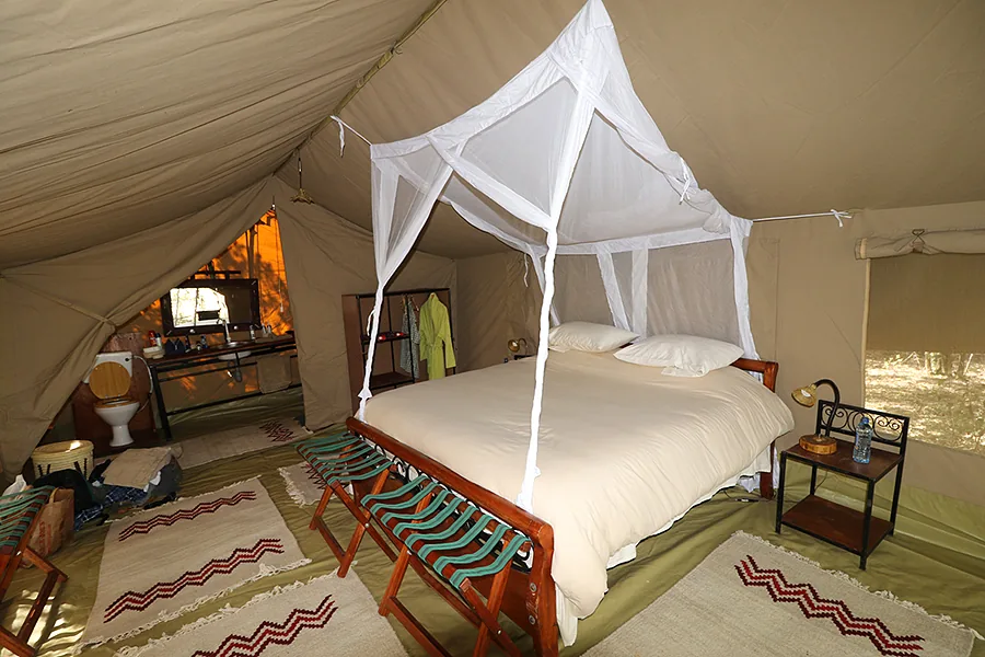 Safari tent bedroom with mosquito-net canopy bed and bedside table at Kaboso Safari Camp.