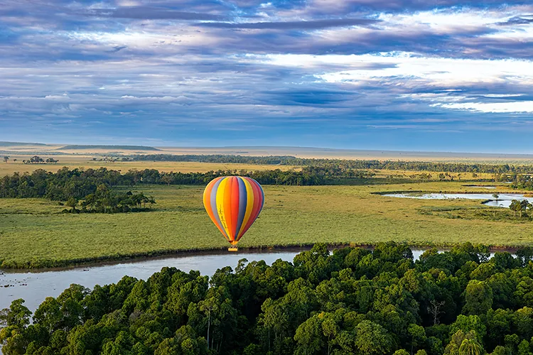 Colorful hot air balloon flying over a winding river and green plains.