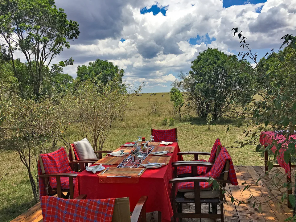 Outdoor dining table with red cloth set beside open savannah at Kaboso Safari Camp.