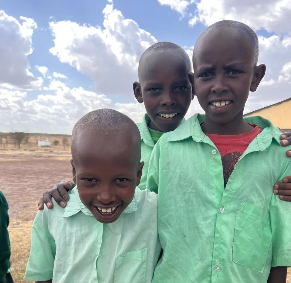 Three boys in green school shirts smiling outdoors.