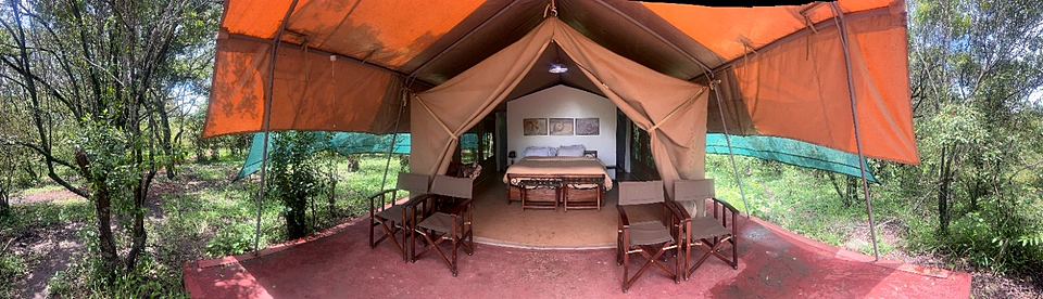 Wide panoramic view of an open safari tent with deck chairs and forest surroundings at Kaboso Safari Camp.